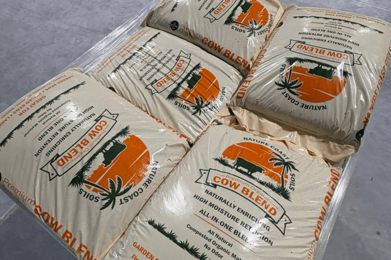 Six bags of "Cow Blend" garden soil, stacked on a pallet. The bags are labeled as naturally enriched, high-moisture retention soil blend for planting.