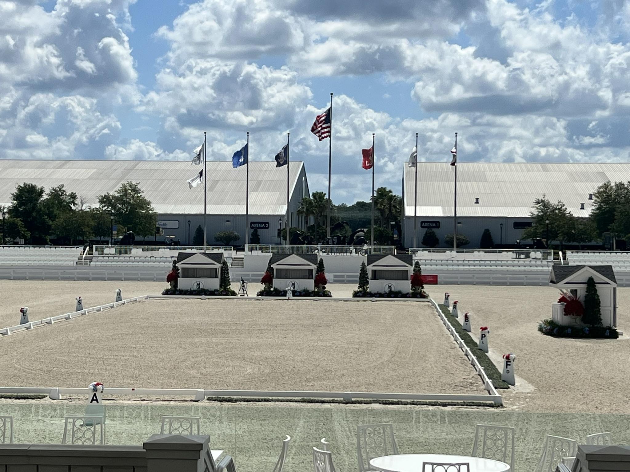 An outdoor equestrian arena with decorated judge booths, flags flying overhead, and white buildings in the background under a partly cloudy sky—located near a leading organic soil producer in North Florida.