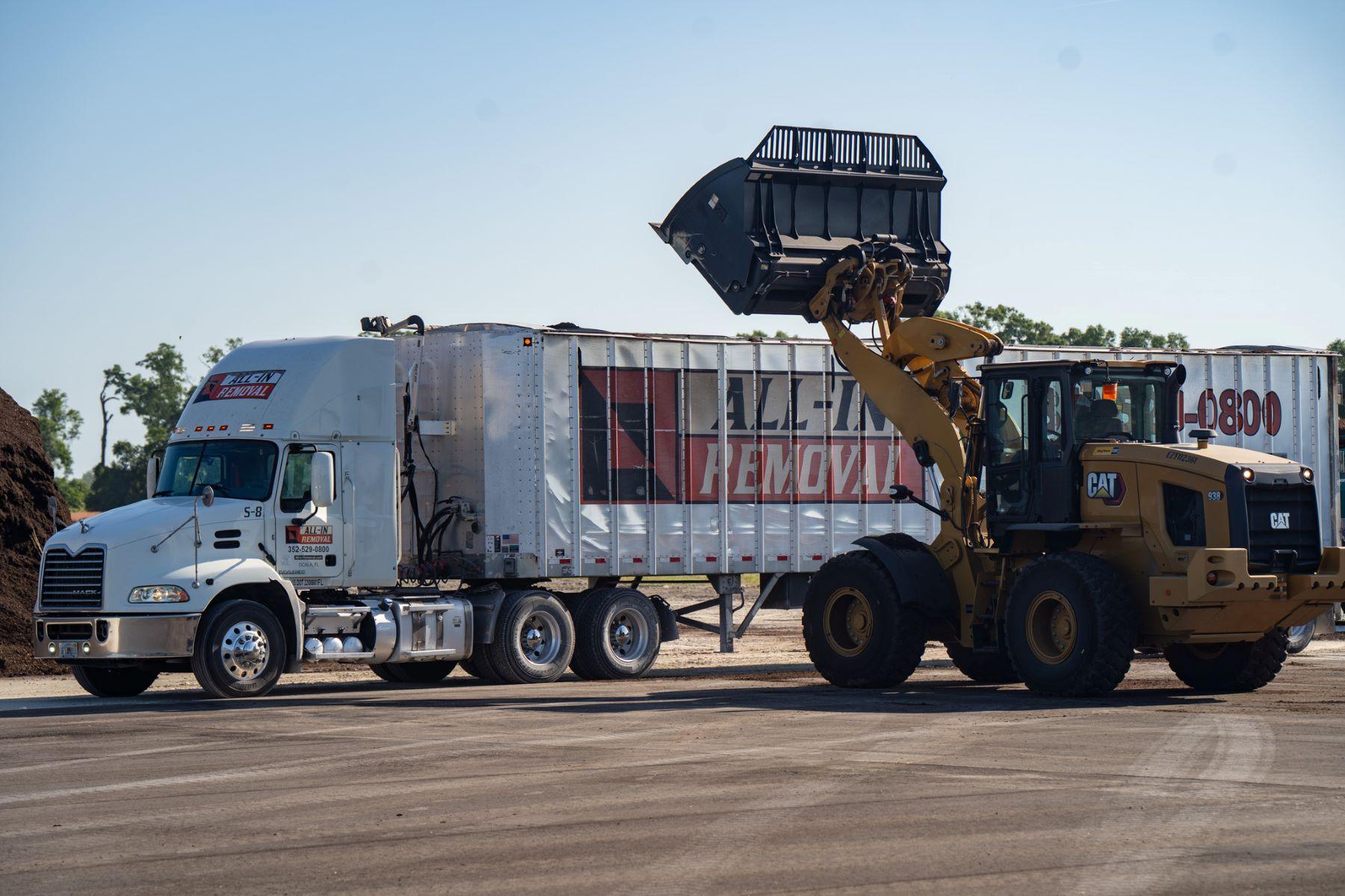 A front loader dumps material into a large trailer truck marked "ALL-STAR REMOVAL" at an outdoor industrial site for an organic soil producer in North Florida.